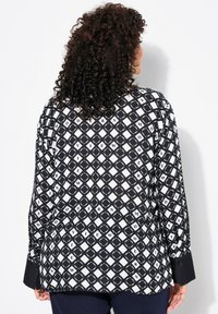 Camicia a righe bianco e nero, con un design a rombi e testo. Maniche lunghe con polsini abbottonati, tessuto dalla texture liscia.