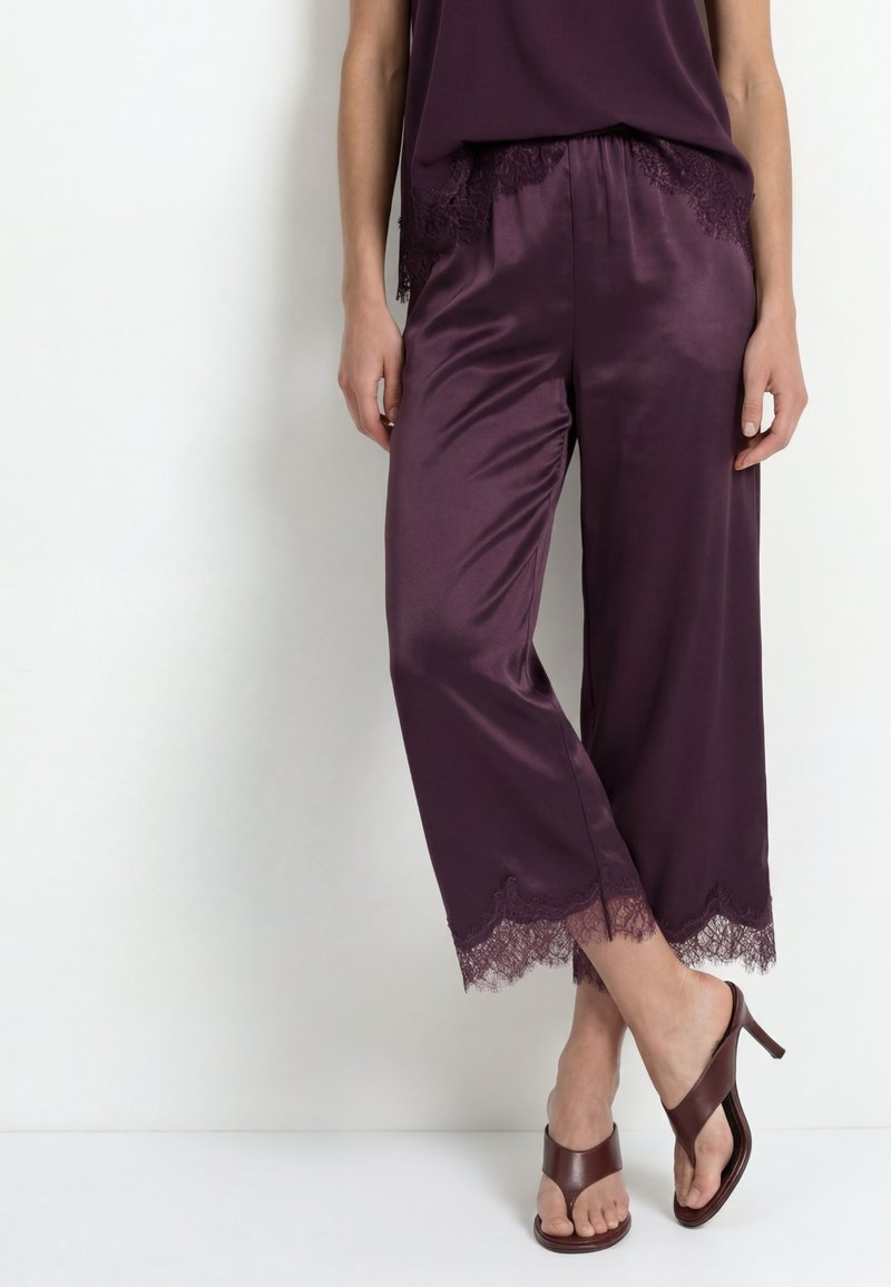 Woman wearing dark purple satin cropped pants with lace trim and matching top, paired with brown open-toe heeled sandals.