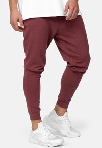 Bordowe dresowe spodnie z tapered legs i ściągaczami, zestawione z białymi sportowymi trampkami z siateczki i skórzanymi detalami.