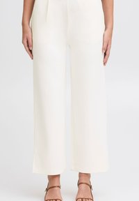 Pantalons larges en crème fabriqués dans un matériau doux avec une texture lisse. Présentent une coupe droite et des détails de couture subtils à l'ourlet.