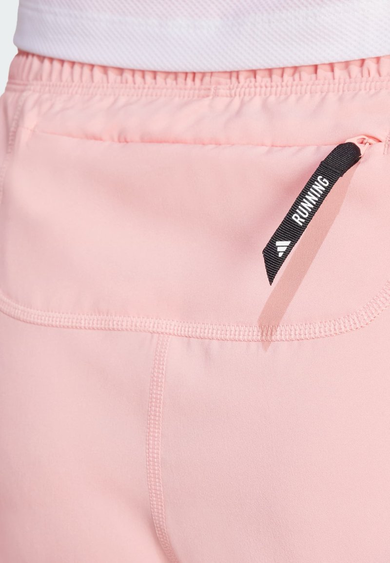 Hellrosa Laufshorts verfügen über einen dehnbaren Bund, eine Gesäßtasche mit einem schwarzen Reißverschluss und sichtbare Nähte entlang der Kanten.