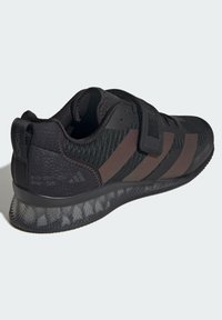 Czarny but sportowy z teksturowaną cholewką z siateczki, paskiem na rzep i brązowymi akcentami. Posiada przezroczystą, wzorzystą podeszwę oraz logo.