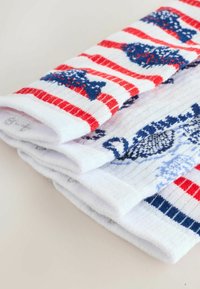 Opgevouwen witte sokken met rode strepen en blauwe vispatronen op een lichte ondergrond.