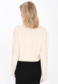 Pulover scurt, de culoare crem deschis, cu mâneci bufante și tiv ribbed. Textură moale și luciu subtil. Fără modele sau embellishments vizibile.