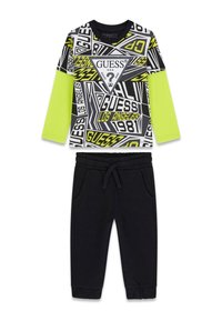 Zweiteiliges Outfit mit einem schwarzen, gemusterten Langarmshirt mit neongrünen Akzenten und schwarzen, zulaufenden Jogginghosen mit elastischem Bund.