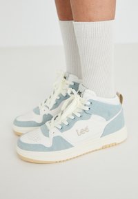 Sapatilhas altas em azul claro e branco, com tecido texturizado e detalhes lisos, apresentando um logo e atacadores em cor creme. Sola de borracha.