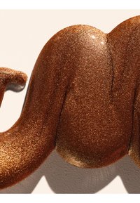 Gros plan d'une sculpture en bronze brillante et texturée avec des courbes arrondies et lisses et une queue enroulée projetant une ombre sur une surface beige.