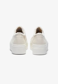Baskets blanches en toile avec une semelle plateforme texturée blanche et un col duveteux blanc. La vue arrière montre un design minimaliste et des lignes épurées.