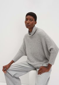Hellgrauer Rollkragenpullover, lockere Passform mit Rippenabschlüssen, kombiniert mit hellgrauen weiten Hosen. Strukturierter Strickstoff.