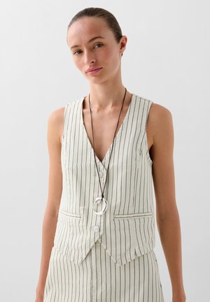 Light beige striped vest with deep V-neck, featuring buttons and two pockets. Paired with a long necklace with circular accent.