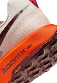 Nærbillede af sålen på en hvid og orange Nike ZoomX sko med sort swoosh logo og gul Vibram branding på dækket.