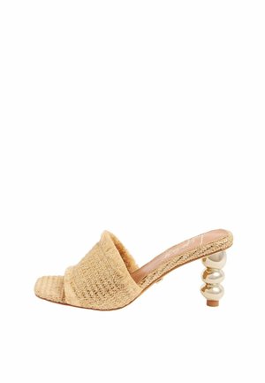 Beżowe plecione mule z odkrytymi palcami, szerokim paskiem i ozdobnym złoconym, piętą w kształcie kulki, widziane z boku.