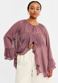 Genomskinlig, lavendelfärgad blus med volangärmar och draperad front, med rund halsringning och mjukt, flödande tyg. Matcher med ljusa byxor.