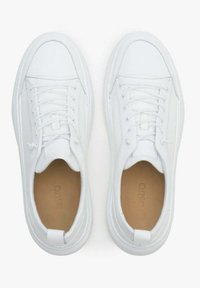 Białe trampki wykonane z gładkiej skóry, z okrągłym czubkiem, sznurowanym zapięciem i lekko podniesioną gumową podeszwą. Wnętrze ma brązowe akcenty.