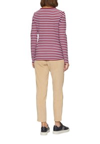 Langermige, geribbelde top met maroon- en witte horizontale strepen, gecombineerd met beige corduroy broek en donkere sneakers met witte zolen.