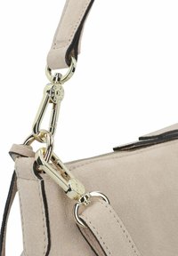 Close-up van een beige suède handtas met een gladde textuur, zwarte afwerkingen en gouden hardware met een sluitingdetail.
