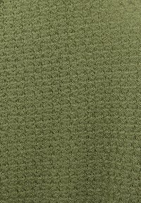 Zielona dziana tkanina z delikatnym, koronkowym wzorem, zawierającym małe otwory i fakturowane ściegi.