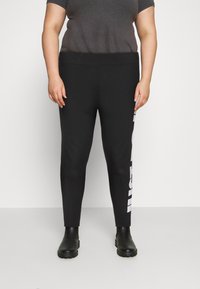 Svarta leggings med hög midja, med en vit logotypdetalj på vänster sida, tillverkade av stretchigt material för komfort.