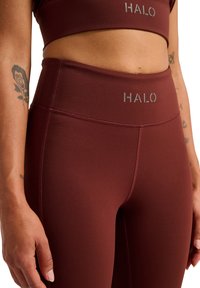 Burgundy träningsbyxor med hög midja, slät yta och en "HALO"-logotyp i grått fram. Den åtsittande designen förbättrar rörligheten.