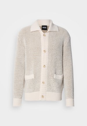 Beige teksturert cardigan med knappelukking foran, bred krage, to frontlommer og ribbede mansjetter. Materialet virker mykt og behagelig.
