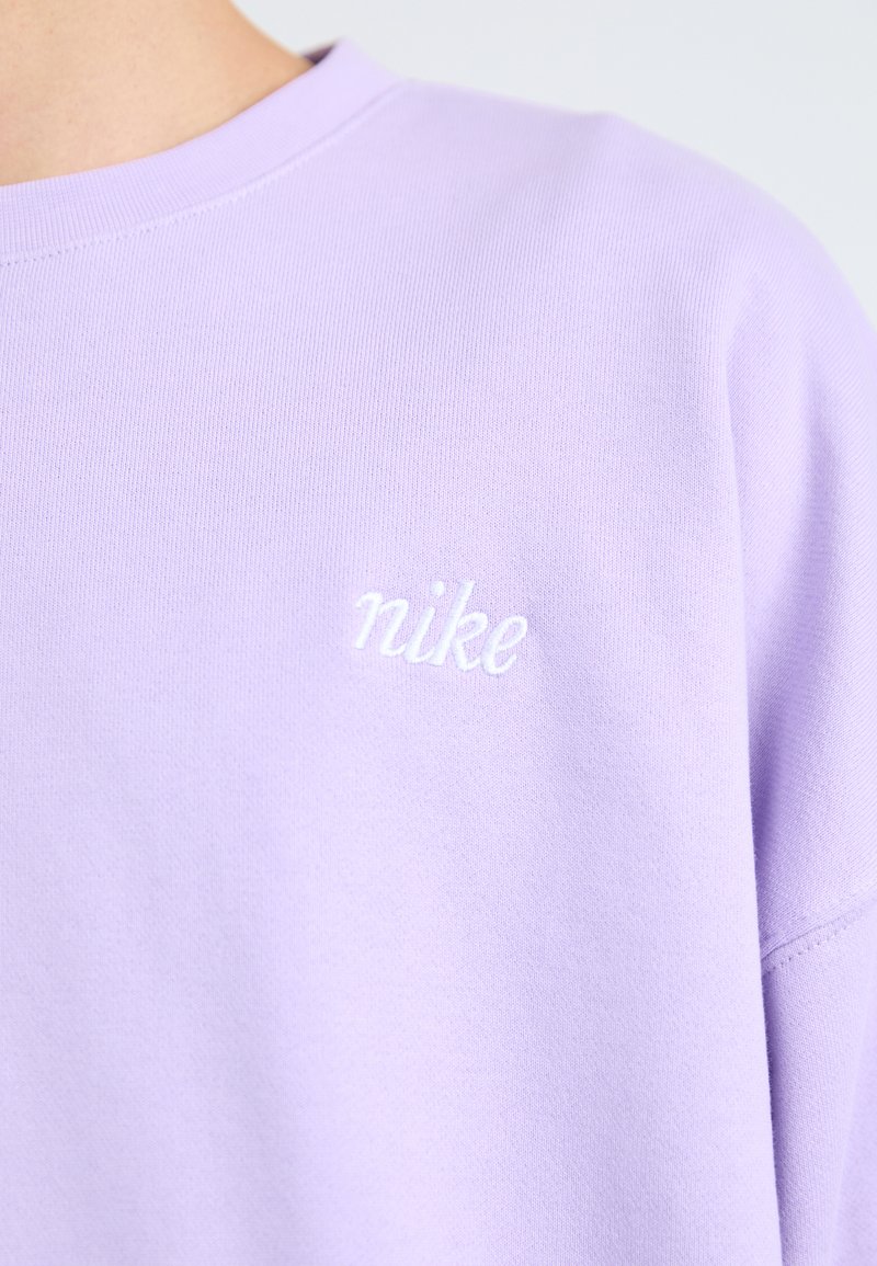 Sweatshirt violet en tissu doux, avec un col rond et un logo "nike" brodé en blanc sur la poitrine. Texture lisse, coupe décontractée.