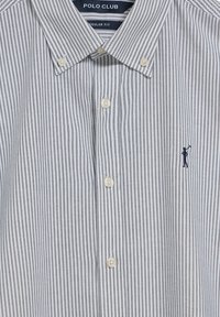 Camicia a righe con bottoni in blu navy e bianco, realizzata in cotone. Presenta un colletto a punta, una vestibilità regolare e un piccolo logo sul lato sinistro del petto.