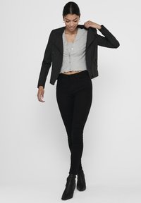 Zwarte faux leren motorjack over een grijze cropped top met geschulpt rand en knopen, gecombineerd met zwarte skinny jeans en enkellaarsjes.