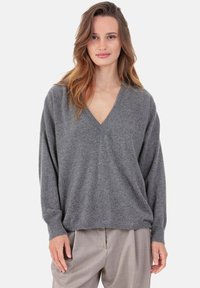 Pull gris à col en V en tissu doux, avec manches longues et coupe décontractée, accompagné d'un pantalon ample gris clair.