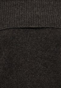 Gros plan d’un tissu tricoté gris charbon avec une texture côtelée en haut et une texture plus douce en dessous.