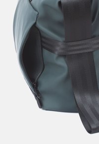 Grüne wasserdichte Reisetasche mit strukturiertem Finish, ausgestattet mit einer Reißverschlusstasche und schwarzen Trageriemen für sicheren Transport.