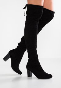 Bottes noires cuissardes en daim doux, avec un talon bloc texturé et un cordon de serrage en haut pour un ajustement réglable.
