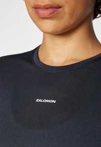 Schwarzes Sport-T-Shirt aus strukturiertem Stoff. Hat einen Rundhalsausschnitt und ein kleines weißes "SALOMON"-Logo auf der Vorderseite.