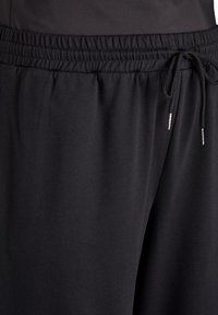 Schwarze Sporthose mit elastischem Bund, Kordelzugverschluss und glatter Stofftextur. Keine Muster oder zusätzlichen Akzente sichtbar.