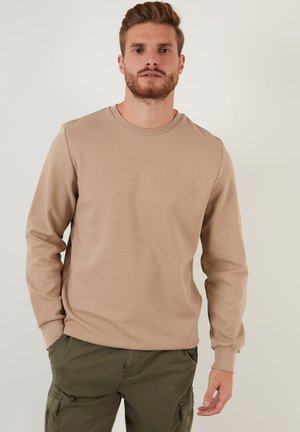 Sudadera de manga larga color marrón claro con cuello redondo y puños acanalados, presentada con pantalones cargo color verde oliva sobre un fondo neutro.