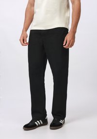 Pantalones rectos negros confeccionados en una mezcla de algodón, con bolsillos sencillos y costuras en contraste. Combinados con zapatillas negras con rayas blancas.