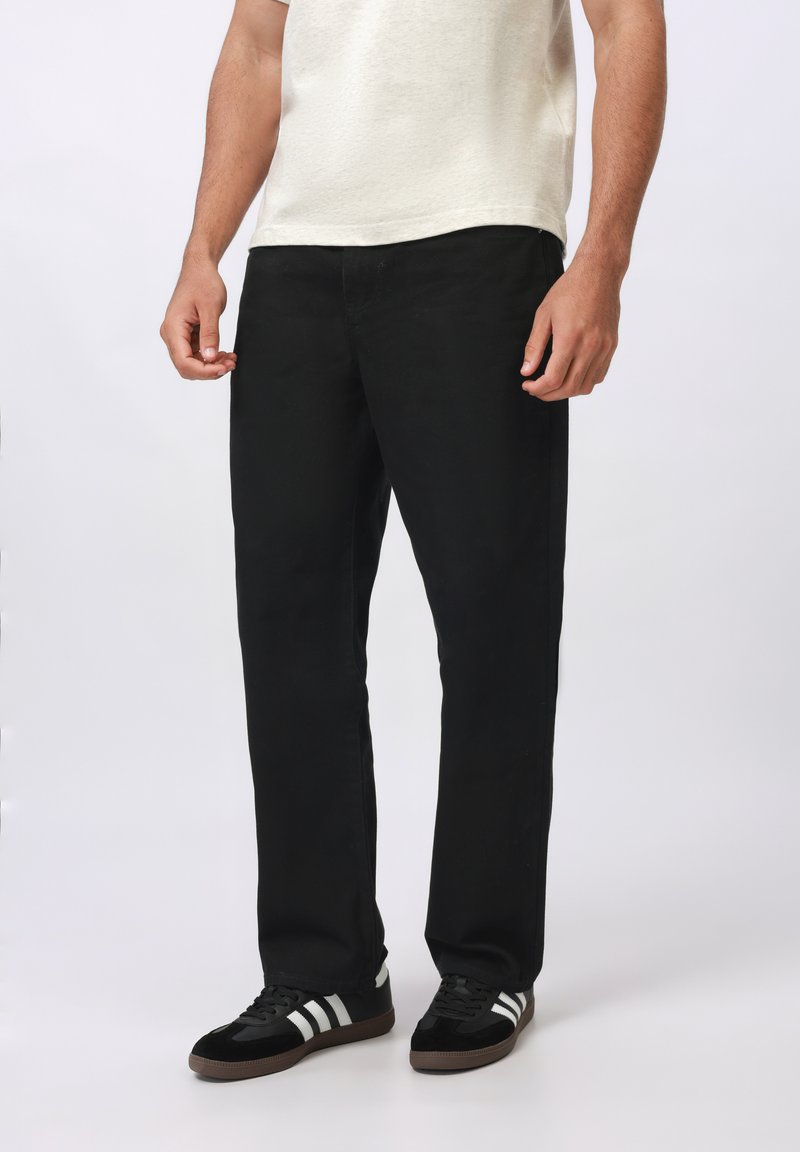 Pantalones rectos negros confeccionados en una mezcla de algodón, con bolsillos sencillos y costuras en contraste. Combinados con zapatillas negras con rayas blancas.