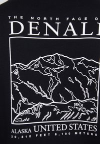 T-shirt nera con una grafica a contorno bianco delle montagne del Denali, con testo che indica la posizione e i dettagli sull'elevazione sottostante.
