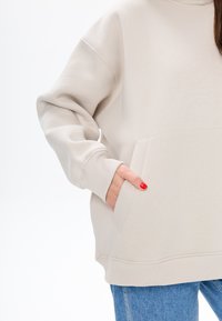 Felpa beige oversize con tasca a marsupio, polsini e orlo a costine; realizzata in morbido materiale misto cotone, presenta una texture liscia.