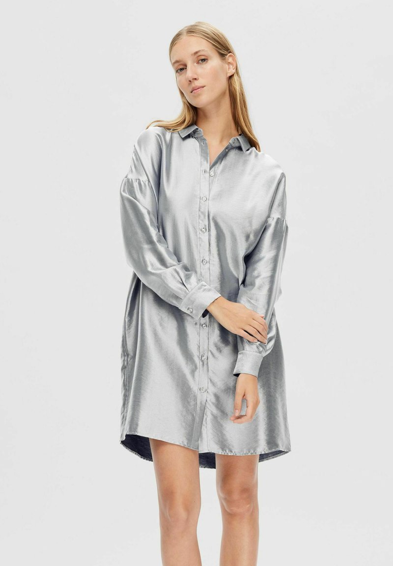 Robe chemise en satin argenté avec un design à boutons, manches longues et ourlet arrondi. Texture lisse avec un léger éclat.