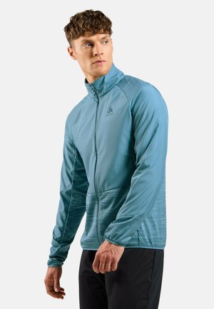 Light blue zip-up jacket with a textured lower half. Features a stand collar and logo on the chest. Made of lightweight, breathable material.