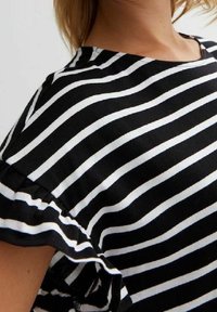 Mustat ja valkoiset raidalliset topit, joissa on lyhyet röyhelöhiha. Kangas näyttää sileältä. Raidat ovat tasaisesti sijoitettuja ja voimakkaita kontrastiltaan.