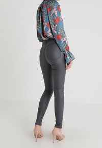 Jeans skinnies de cintura alta en gris oscuro con una textura suave y bolsillos traseros, combinados con una blusa floral de manga larga y tacones nude.