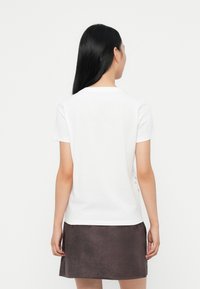 Hvit kortermet t-skjorte med rund hals, vist fra baksiden. Glatt bomullsstoff, kombinert med et mørkegrå skjørt. Enkelt og minimalistisk design.