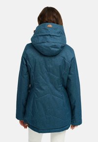 Niebieska pikowana kurtka z kapturem, wykonana z teksturowanego materiału z naszywką z logo na plecach. Długie rękawy i krój sięgający do bioder.