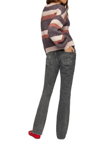 Strickpullover mit gestreiftem Muster in lila, rosa und creme, kombiniert mit grauen Denim-Jeans. Rote Ballerinas runden das Outfit ab.