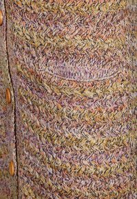 Pletený cardigan s vzorem rybí kosti v žlutých, růžových a fialových odstínech. Obsahuje náprsní kapsu a béžové knoflíky. Strukturovaná tkanina.