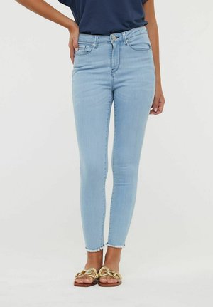 Jeans skinny bleu clair en denim à taille haute, avec un ourlet brut et un design classique à cinq poches. Assortis à des sandales dorées.