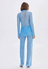 Ensemble deux pièces en dentelle bleu ciel comprenant un haut à manches longues et un pantalon assorti. Le tissu est transparent avec des motifs floraux et une coupe ajustée.