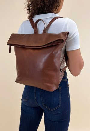 Brown leather backpack with a fold-over flap, zip closure, and two shoulder straps. Smooth texture, minimal design, and no visible hardware.