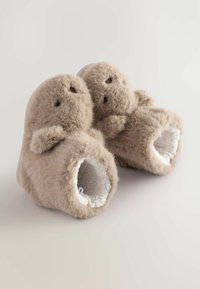 Flauschige beige Hausschuhe mit runder Form, plüschiger Außenseite und weichem weißen Innenfutter. Mit kleinen Ohren und gestickten Gesichtszügen.